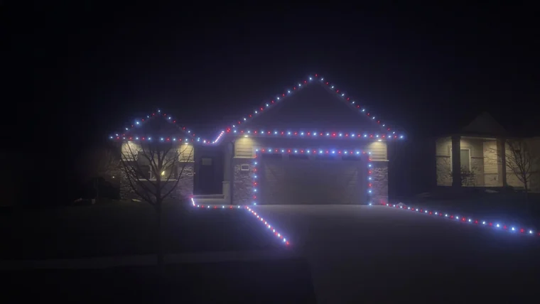 Traditional C9 Christmas light bulbs in red, white and blue along the roofline, garage trim and driveway path of a ranch home in Lincoln, NE
